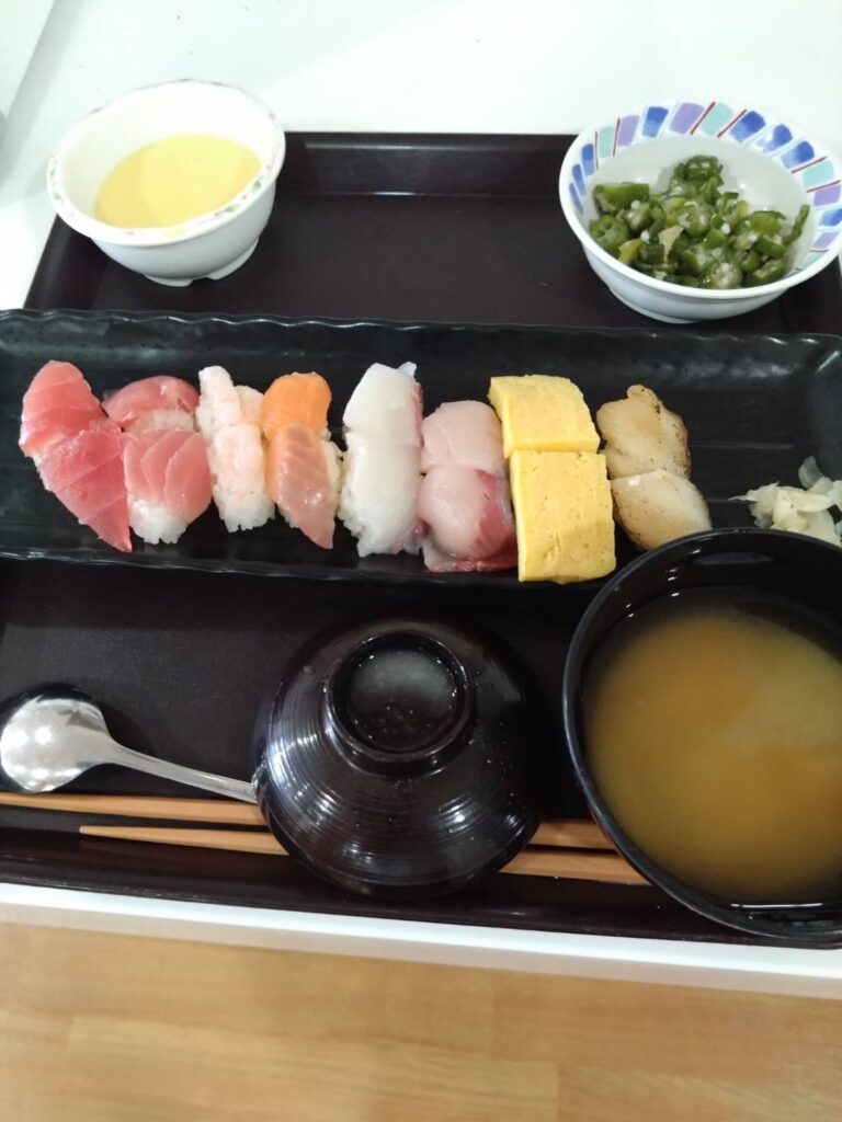 握り寿司定食。多種類のネタが黒いトレーに並び、汁物と薬味が添えられている